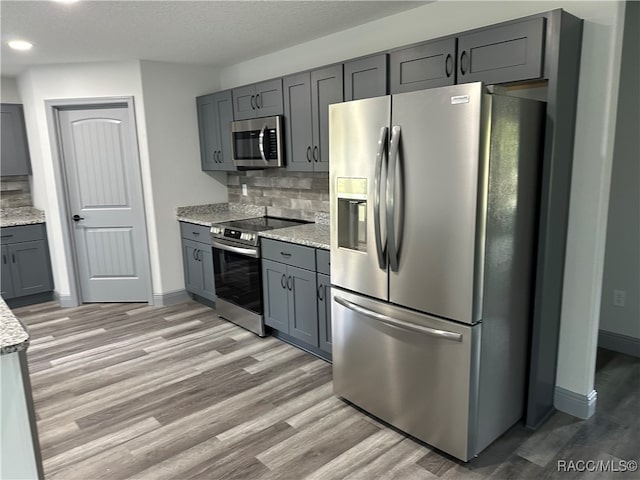 kitchen with tasteful backsplash, light stone countertops, gray cabinets, and stainless steel appliances