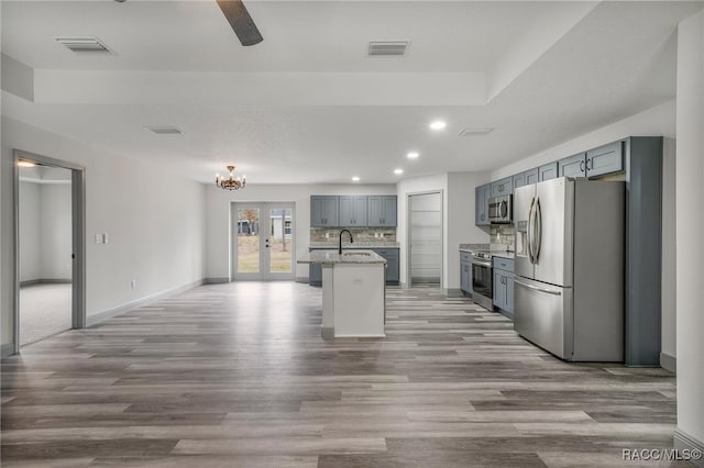 kitchen featuring light hardwood / wood-style floors, stainless steel appliances, backsplash, a kitchen island with sink, and sink