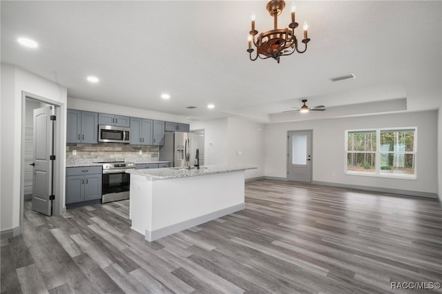 kitchen featuring appliances with stainless steel finishes, wood-type flooring, ceiling fan with notable chandelier, and backsplash