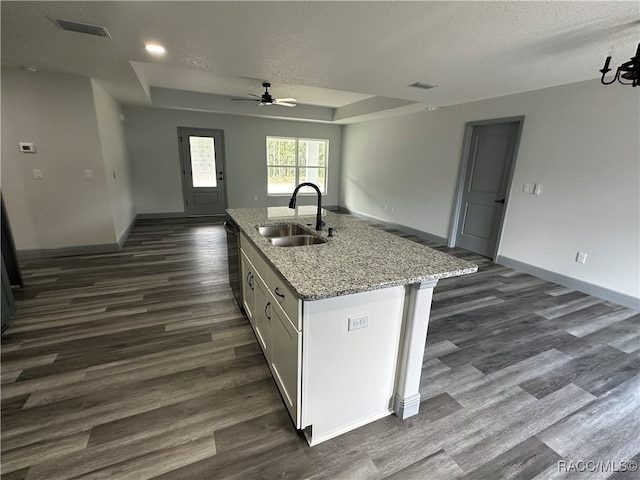 kitchen with ceiling fan, a tray ceiling, a kitchen island with sink, white cabinets, and sink