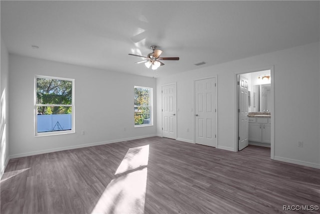 unfurnished bedroom with ceiling fan, dark hardwood / wood-style floors, two closets, and ensuite bath