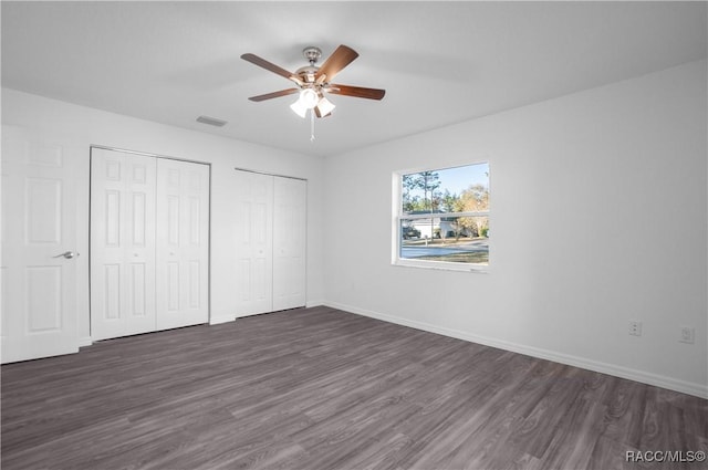 unfurnished bedroom featuring dark hardwood / wood-style floors, two closets, and ceiling fan