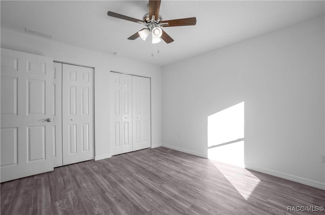 unfurnished bedroom featuring ceiling fan, hardwood / wood-style floors, and two closets