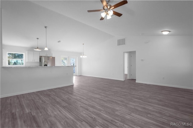 unfurnished living room featuring dark wood-type flooring, plenty of natural light, vaulted ceiling, and ceiling fan with notable chandelier