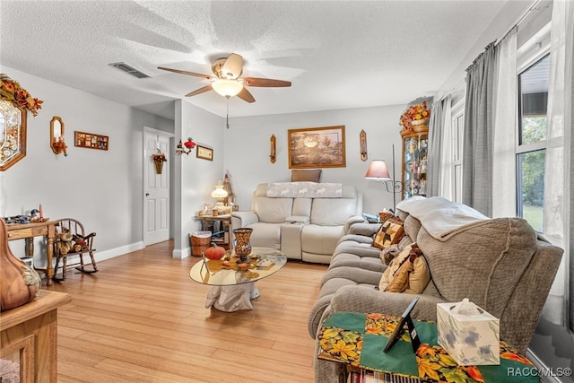 living room with ceiling fan, light wood-type flooring, and a textured ceiling