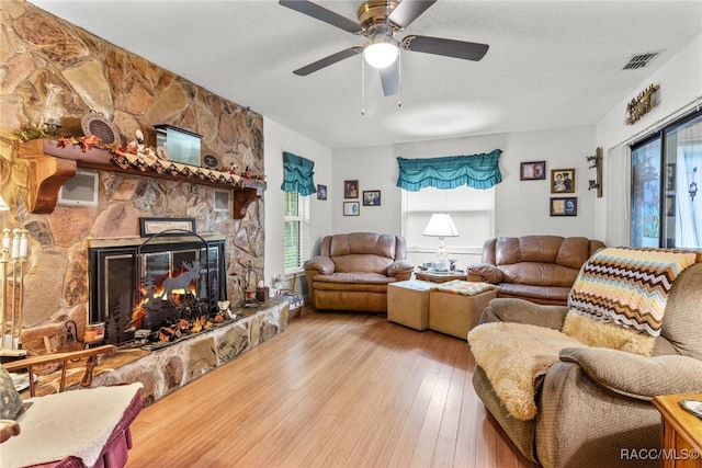 living room with a fireplace, ceiling fan, light hardwood / wood-style flooring, and a textured ceiling