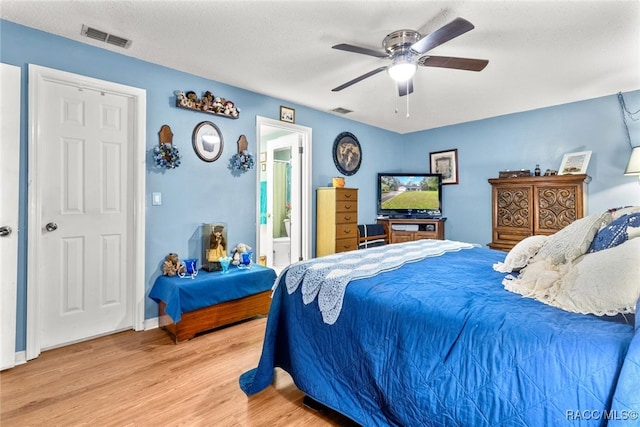 bedroom with ceiling fan, light wood-type flooring, a textured ceiling, and connected bathroom