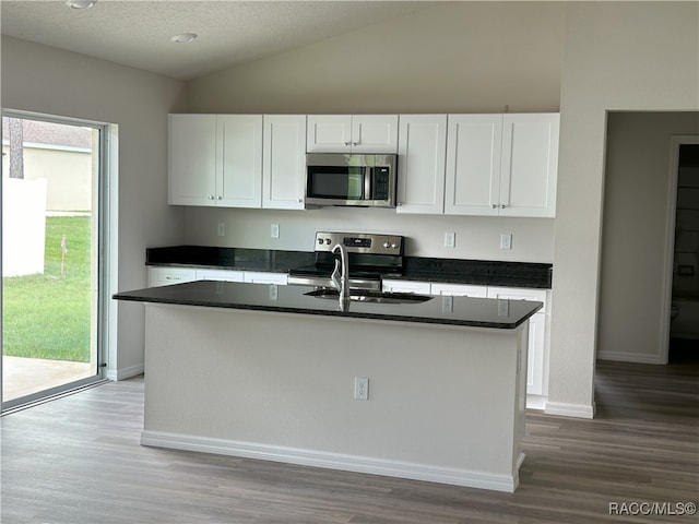 kitchen featuring stainless steel appliances, hardwood / wood-style flooring, white cabinetry, lofted ceiling, and an island with sink