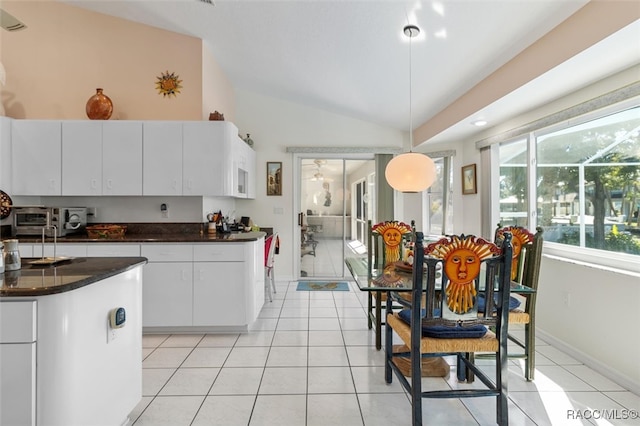 kitchen with pendant lighting, vaulted ceiling, white cabinetry, and light tile patterned floors