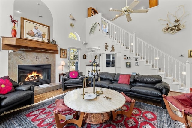 living room with hardwood / wood-style floors, ceiling fan, a tile fireplace, and a high ceiling