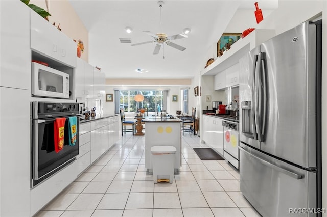 kitchen with light tile patterned floors, white appliances, white cabinetry, and a kitchen island