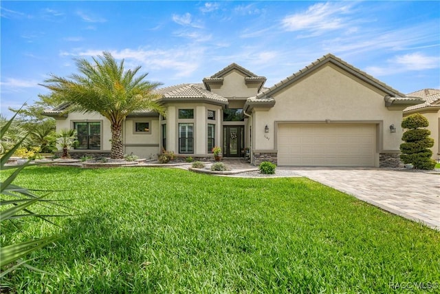 mediterranean / spanish-style house with stucco siding, stone siding, decorative driveway, a front yard, and a garage