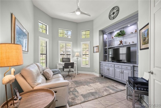 living room featuring light tile patterned floors, baseboards, a ceiling fan, and a towering ceiling