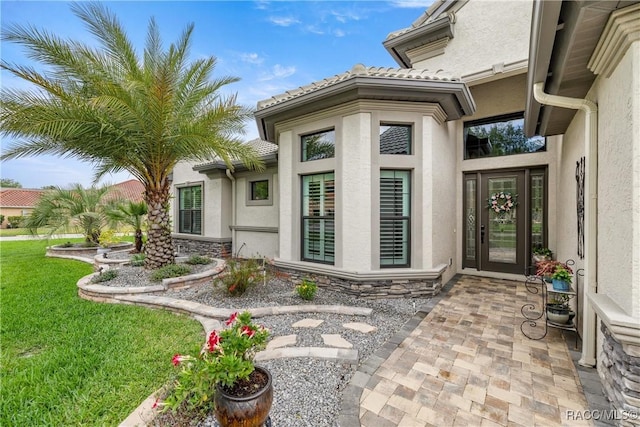 doorway to property with a tiled roof, stone siding, and stucco siding