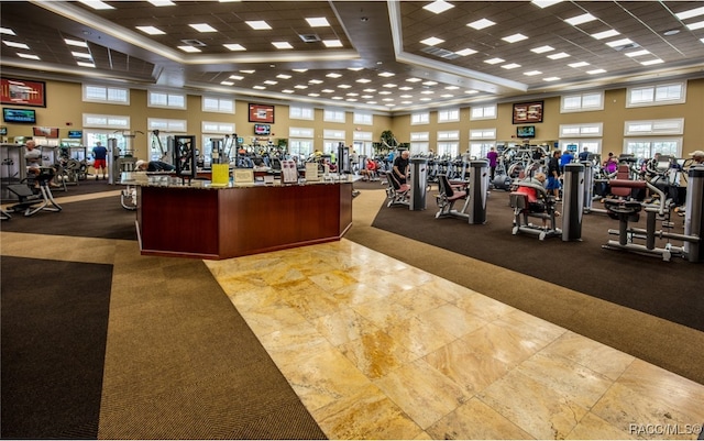 exercise room with a raised ceiling, a paneled ceiling, ornamental molding, and carpet