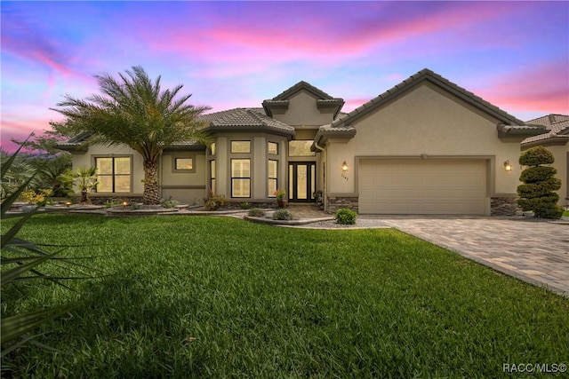 view of front of house with stucco siding, stone siding, decorative driveway, a garage, and a lawn