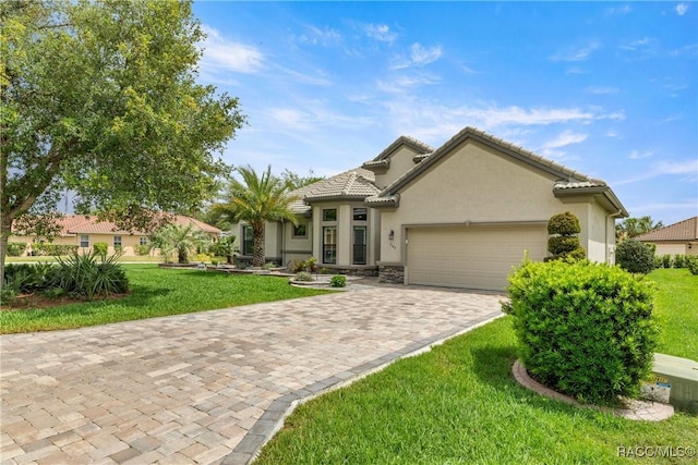 view of front facade featuring a tiled roof, stucco siding, decorative driveway, a front lawn, and an attached garage