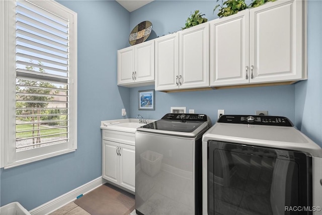 clothes washing area featuring baseboards, washing machine and clothes dryer, a sink, and cabinet space