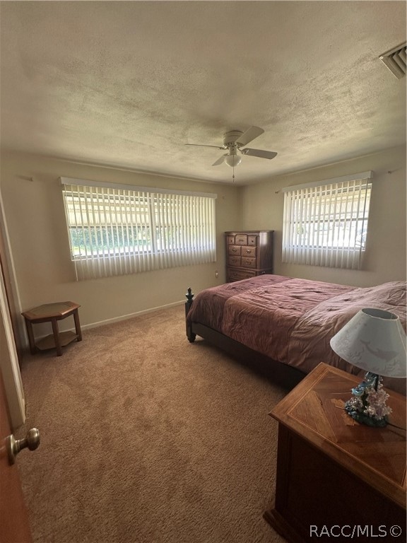 carpeted bedroom with multiple windows, ceiling fan, and a textured ceiling