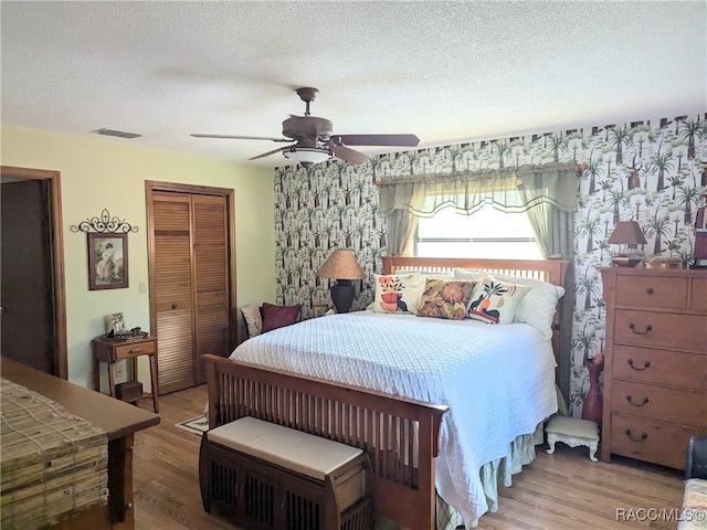 bedroom with a textured ceiling, a closet, ceiling fan, and light hardwood / wood-style floors