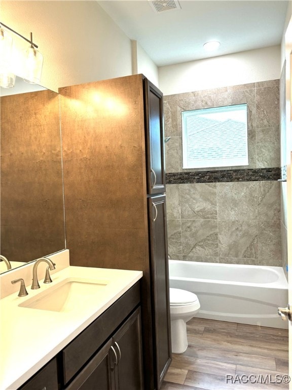 full bathroom with hardwood / wood-style floors, vanity, tiled shower / bath combo, and toilet