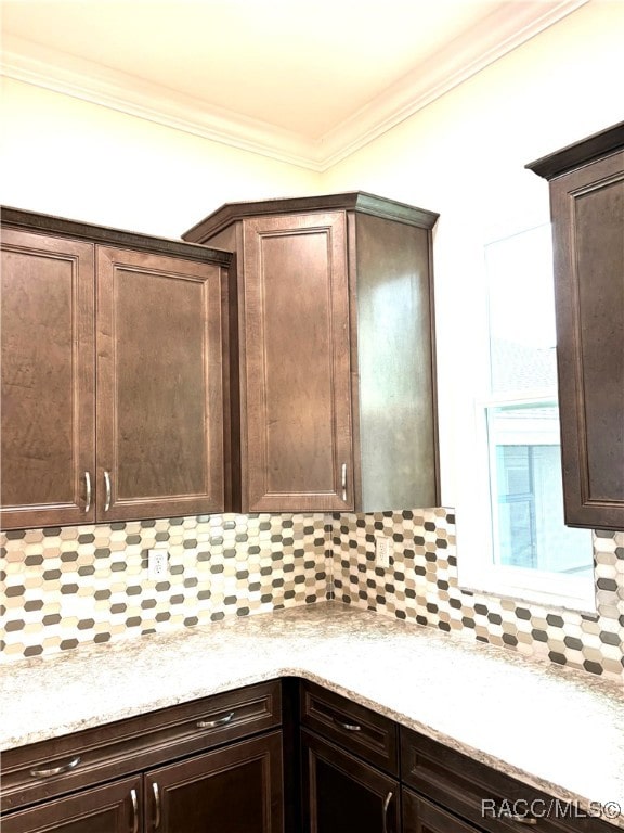 kitchen featuring tasteful backsplash, crown molding, dark brown cabinets, and light stone counters