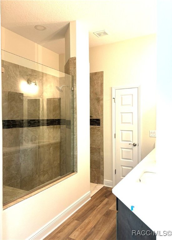 bathroom featuring a textured ceiling, vanity, wood-type flooring, and tiled shower