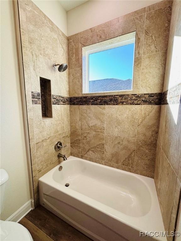 bathroom with tiled shower / bath combo, wood-type flooring, and toilet