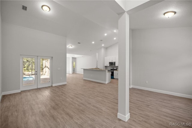 unfurnished living room featuring light hardwood / wood-style floors, french doors, and high vaulted ceiling