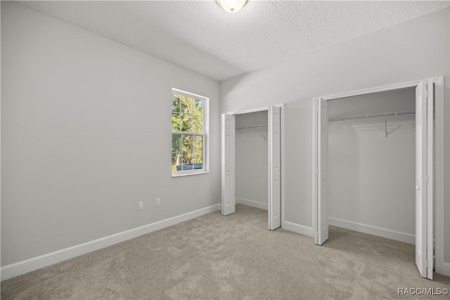 unfurnished bedroom with light colored carpet, multiple closets, and a textured ceiling