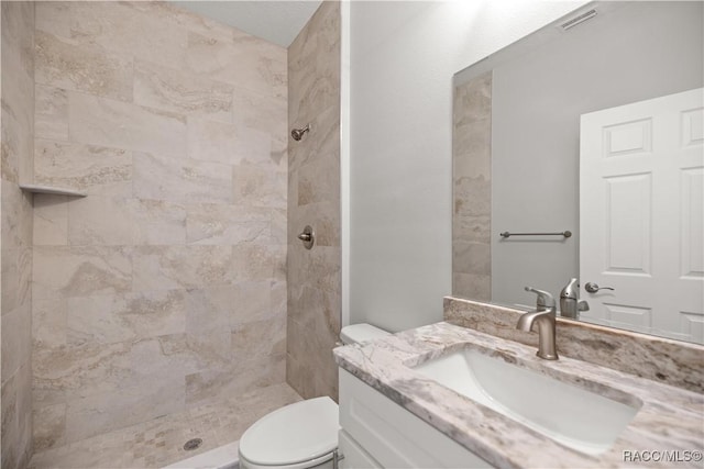 bathroom featuring toilet, tiled shower, and vanity