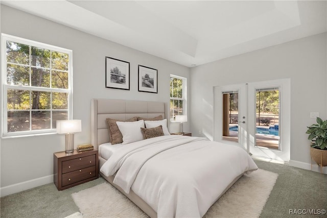 bedroom featuring light carpet, access to exterior, french doors, and a tray ceiling