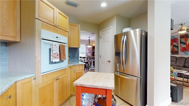 kitchen with oven, stainless steel fridge, backsplash, light tile patterned floors, and light brown cabinets