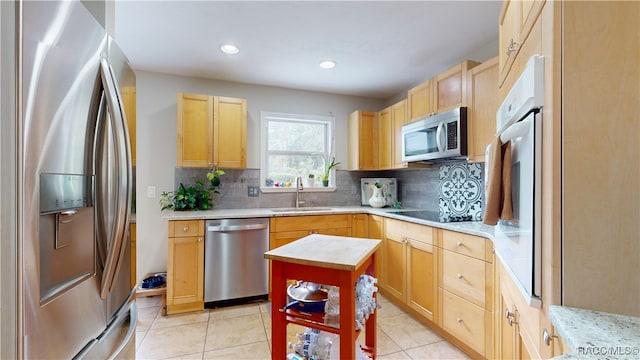 kitchen with light tile patterned flooring, light brown cabinetry, sink, tasteful backsplash, and appliances with stainless steel finishes