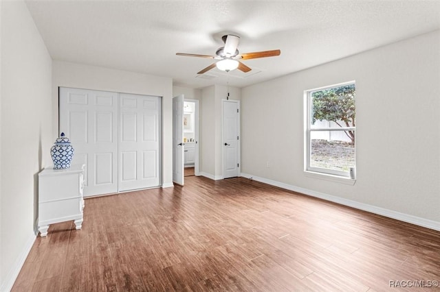 unfurnished bedroom featuring wood-type flooring, a textured ceiling, ceiling fan, and a closet