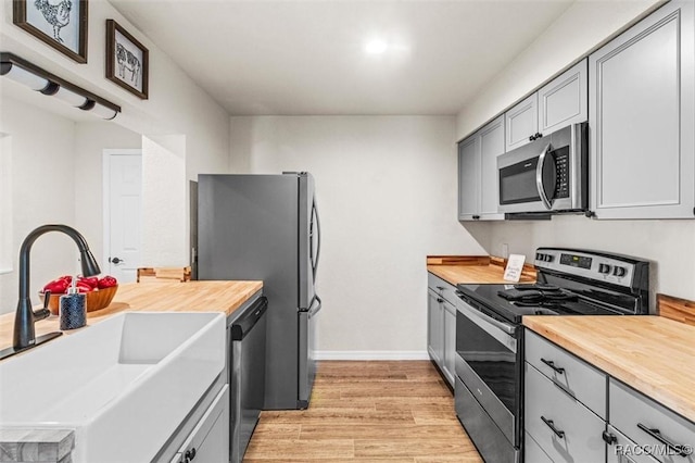 kitchen featuring butcher block counters, sink, light hardwood / wood-style flooring, gray cabinets, and stainless steel appliances