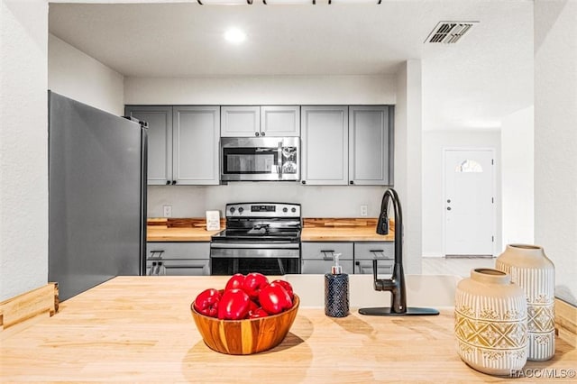 kitchen with wood counters, gray cabinets, and stainless steel appliances