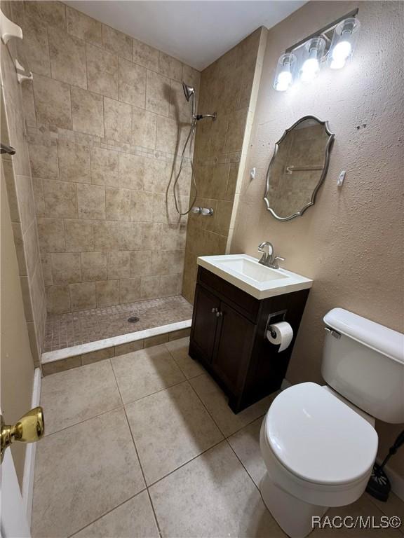 bathroom featuring tile patterned floors, toilet, vanity, and tiled shower