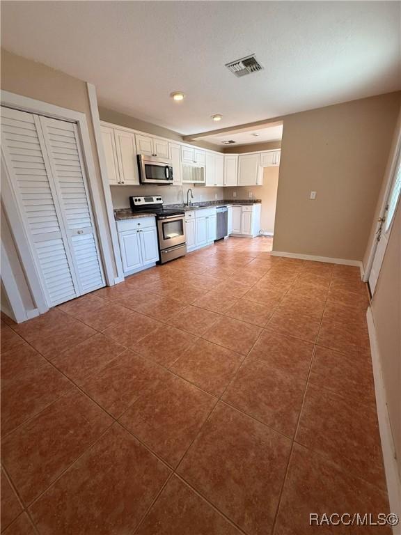 kitchen featuring appliances with stainless steel finishes, sink, white cabinets, and dark tile patterned floors