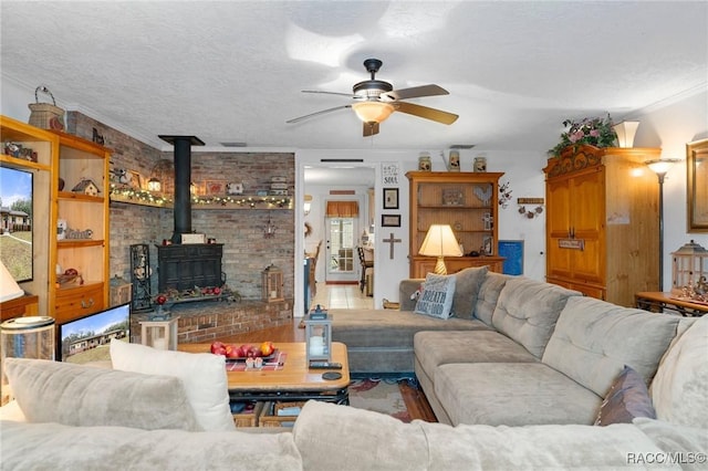 living room with ceiling fan, a wood stove, a textured ceiling, and ornamental molding