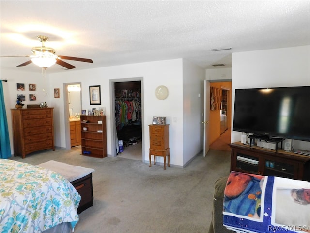 carpeted bedroom featuring connected bathroom, ceiling fan, a textured ceiling, a walk in closet, and a closet