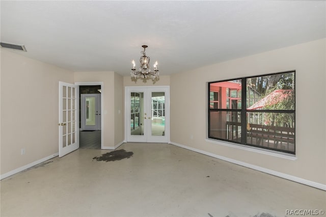 spare room with a chandelier, concrete flooring, and french doors