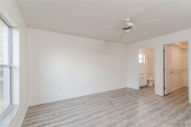 unfurnished bedroom featuring connected bathroom, a walk in closet, a textured ceiling, light wood-type flooring, and a closet