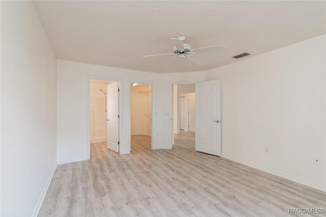 unfurnished bedroom with a closet, a spacious closet, a textured ceiling, and light wood-type flooring