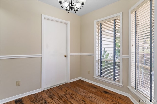 empty room featuring an inviting chandelier, plenty of natural light, and dark wood-type flooring