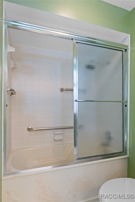 bathroom featuring toilet and combined bath / shower with glass door