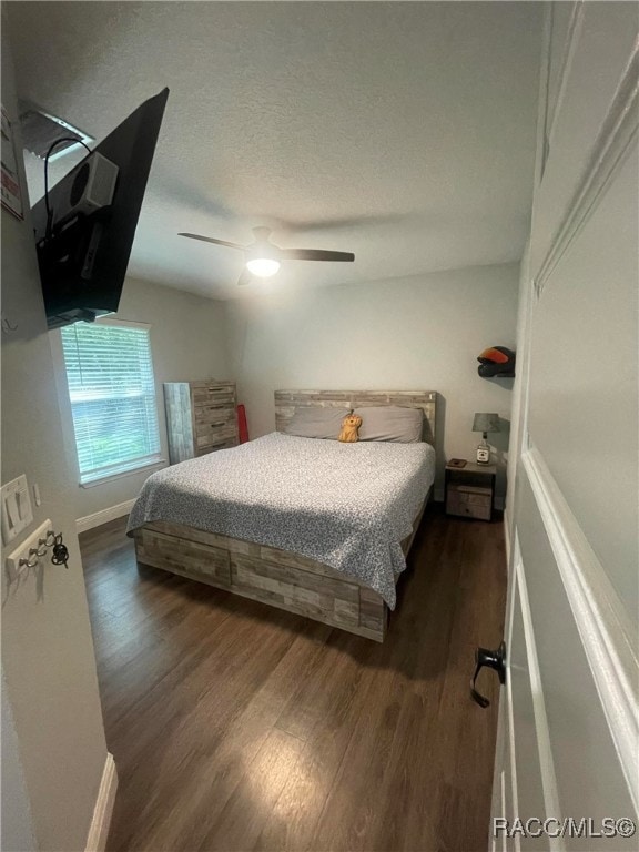 bedroom with a textured ceiling, ceiling fan, and dark wood-type flooring