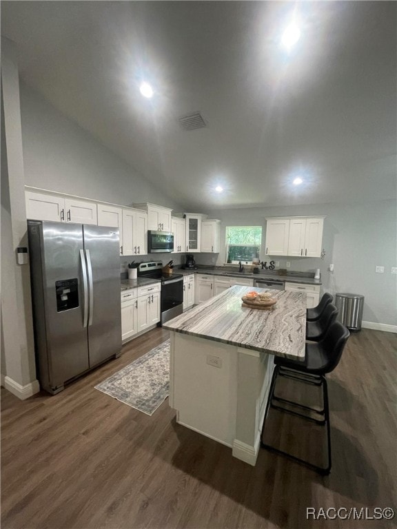 kitchen with dark wood-type flooring, vaulted ceiling, white cabinetry, a breakfast bar area, and stainless steel appliances