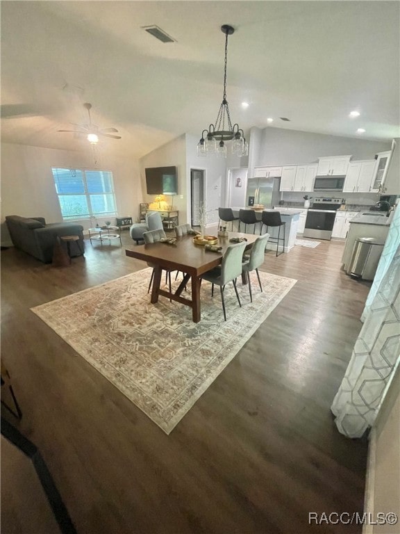 dining area featuring ceiling fan with notable chandelier, dark hardwood / wood-style floors, and vaulted ceiling