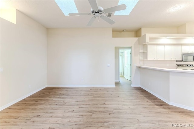 unfurnished living room with ceiling fan, a skylight, and light wood-type flooring